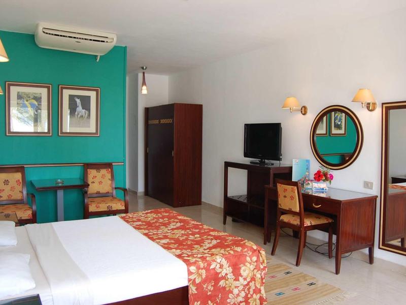 Chambre d'hôtel avec lit double, couvre-lit coloré, bureau et chaises devant un mur vert.