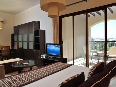Hotel room with bed, TV, seating area, and balcony overlooking outdoors.
