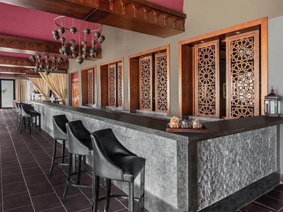 Long bar with black chairs and intricate wooden paneling in a stylish hotel lounge.