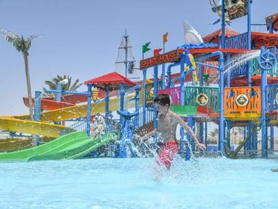 Child plays in a shallow pool area of a colorful water park with slides and water features.