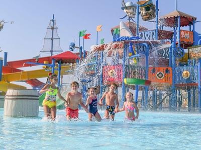 Children playing in a colorful water park with slides and splash structures under a clear sky.
