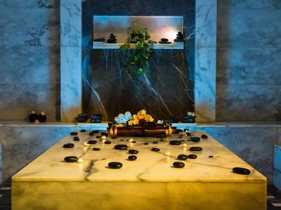 Modern spa room with large stone hot tub, candles, and decorative plants in a serene setting.