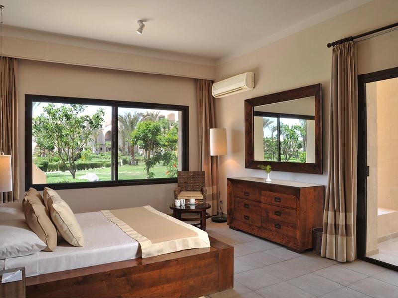 Well-lit hotel room with wooden furniture, large window, and a view of palm trees.
