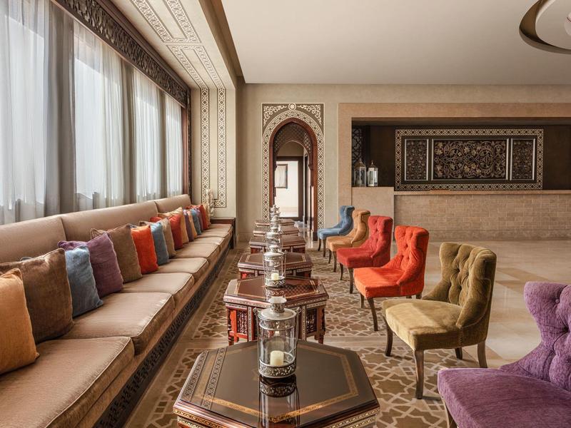 Cozy hotel lounge with colorful armchairs, long cushioned bench by large windows, and decorative lanterns.