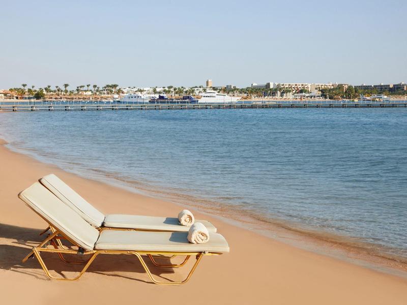 Beach chair on sandy shore beside calm blue sea under clear sky.