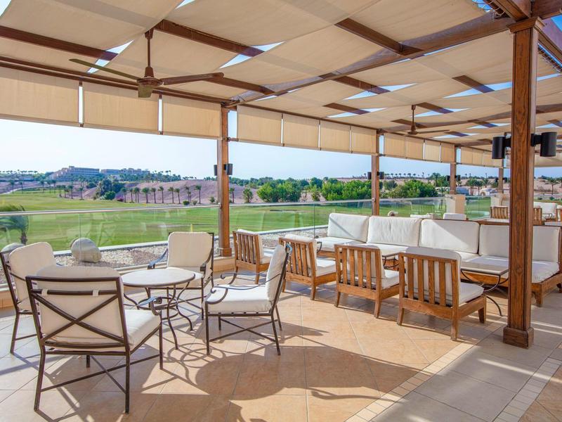Outdoor terrace with tables, chairs, and a shaded pergola overlooking green fields.