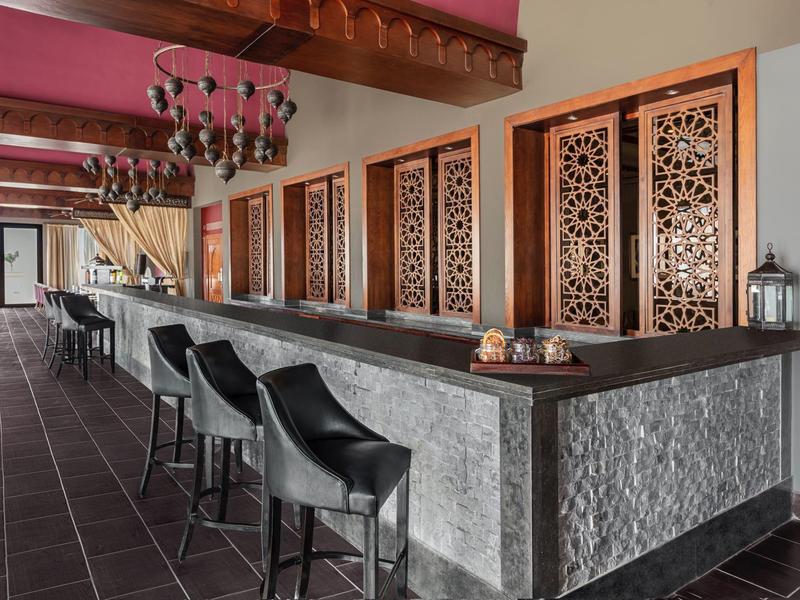 Long bar with black chairs and intricate wooden paneling in a stylish hotel lounge.