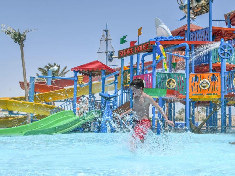 Child splashing in a pool with colorful water slides and play structures in the background.