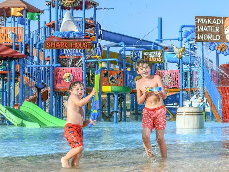 Two boys enjoying shallow water at a colorful water park with slides and play structures.