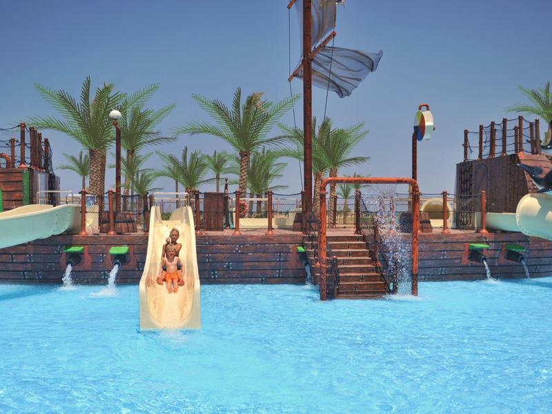 Water slides and palm trees at a tropical hotel pool area under a clear sky.