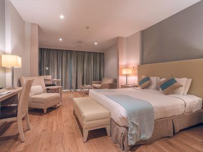 Camera d'hotel moderna con letto matrimoniale, zona salotto e pavimento in legno.