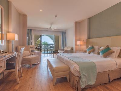 Prostorný hotelový pokoj s manželskou postelí, psacím stolem, posezením a balkonem s výhledem na moře.