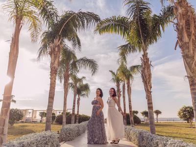 Due donne in abiti estivi camminano su un sentiero fiancheggiato da palme all'aperto.