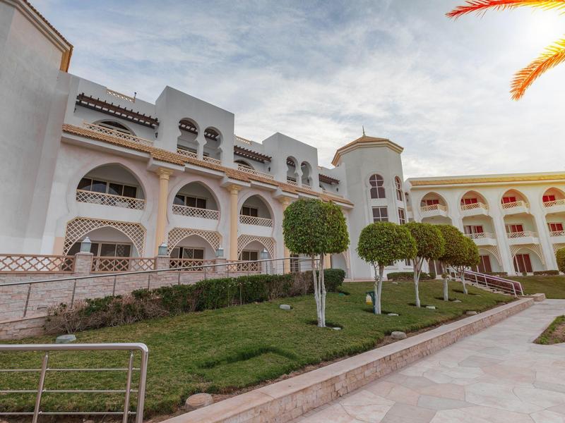 Velká hotelová budova s oblouky a upravenou zahradou pod zataženou oblohou.