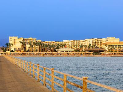 Wide pier leading to a large beachfront hotel under a clear blue sky at sunset.