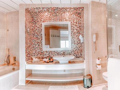 Luxurious bathroom with a large mirror, white bathtub, and decorative brown mosaic wall.