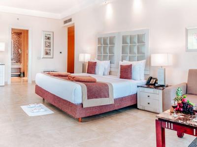 Modern hotel room with double bed, bedside tables, seating area, and decorative artwork.