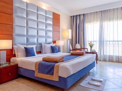 Cozy hotel room with large bed, soft pillows, wooden accents, and bright natural light.