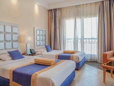 Hotel room with two single beds, purple accents, towels, and a balcony with sheer curtains.