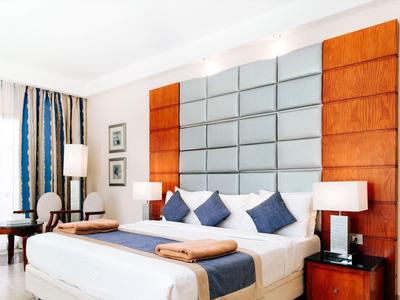 Bright hotel room with large bed, blue and white decor, wooden accents, and elegant curtains.