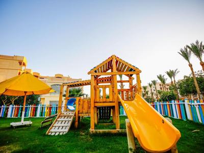 Wooden playground structure with yellow slide and umbrella in fenced grassy area under clear sky.