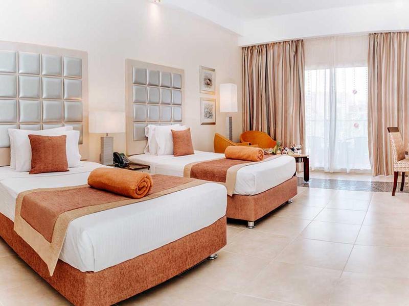 Spacious hotel room with two beds, neutral tones, and large windows with curtains.