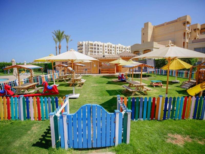 Outdoor kids' play area with slides and colorful fencing at a sunny resort garden.