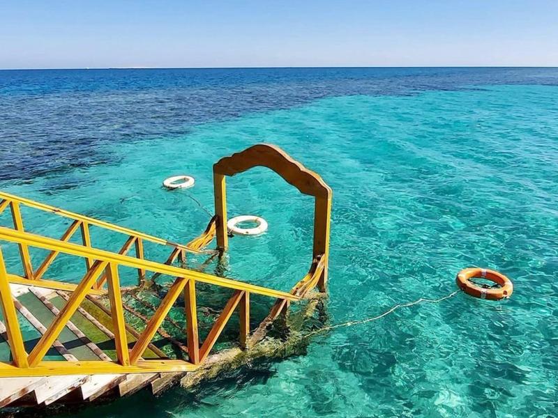 Yellow wooden stairs leading into clear turquoise ocean waters with floating life rings.