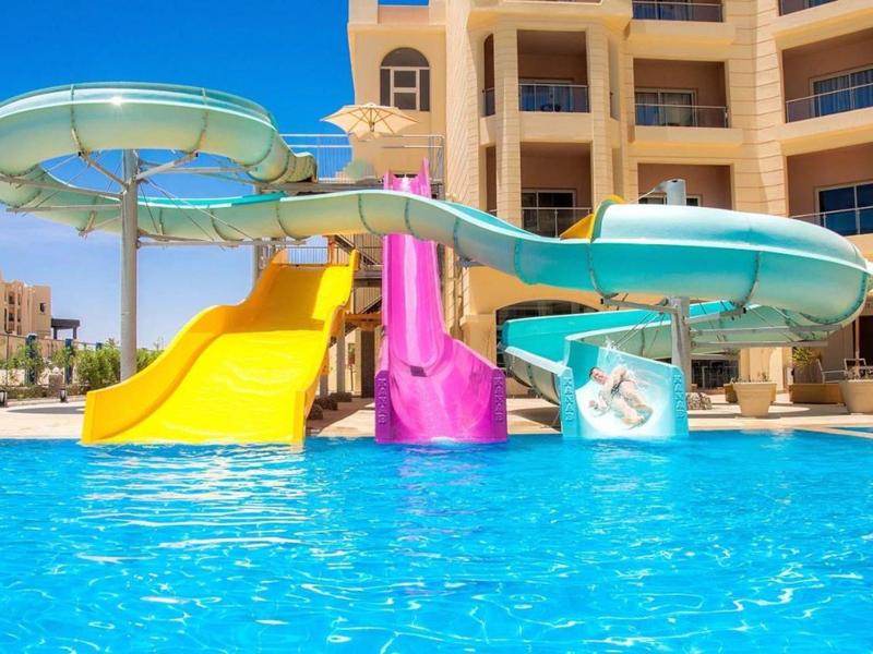 Water slides and a pool in a hotel courtyard under clear skies.