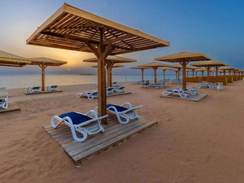 Empty beach chairs and wooden umbrellas line a sandy beach at sunset.