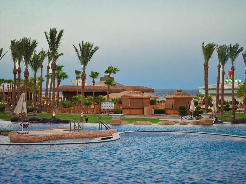 Resort with a large pool, tall palm trees, and terracotta buildings by the sea.