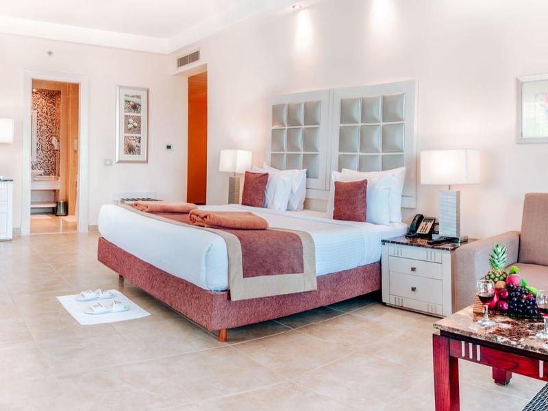 Modern hotel room with double bed, bedside tables, seating area, and decorative artwork.