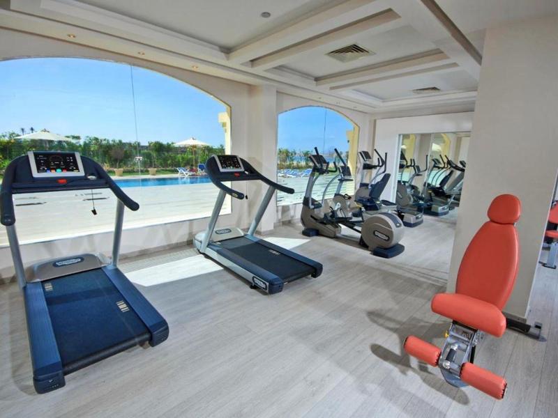 Bright gym with cardio machines and a gym bench overlooking the pool outside.