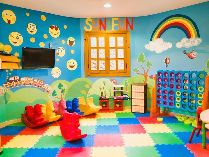 Colorful kids' playroom with emoji wall, foam floor tiles, toys, and a rainbow decoration.