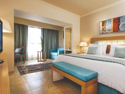 Modern eingerichtetes Hotelzimmer mit großem Bett, Sitzecke, Fernseher und hellem Holzmobiliar.