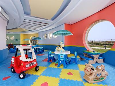 Bunte Kinderspielecke mit Spielautos, Tischen, Stühlen und rundem Fenster an roter Wand.