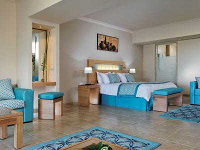 Modernes Schlafzimmer mit Doppelbett, Holzmöbeln und blauen Akzenten in Decke, Kissen und Sitzmöbeln.