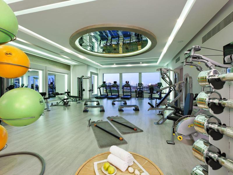 Moderner Fitnessraum mit Hanteln, Laufbändern, bunten Medizinbällen und großem Fenster.