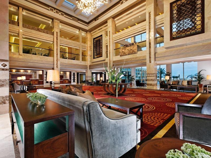 Großer, eleganter Hotel-Lobbyraum mit hohen Decken, Sitzgruppen, Teppichboden und vielen Fenstern.