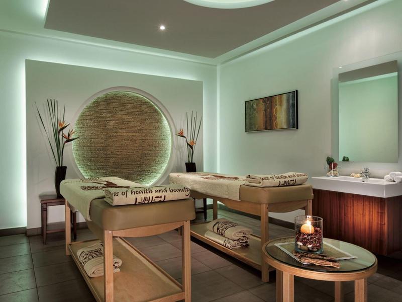 Helles Wellnesszimmer mit zwei Massageliegen, indirekter Beleuchtung und dekorativer Wandgestaltung.