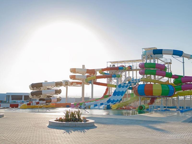 Wasserpark mit bunten, geschwungenen Wasserrutschen unter einem hellen, sonnigen Himmel.