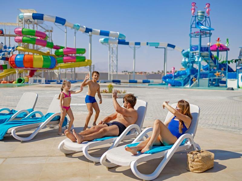 Menschen entspannen und spielen an einem sonnigen Wasserpark mit bunten Rutschen im Hintergrund.