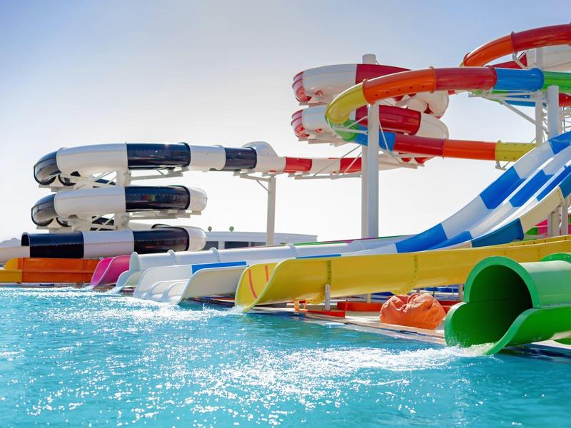 Vielfarbige, lange Wasserrutschen führen ins blaue Schwimmbecken unter klarem Himmel.