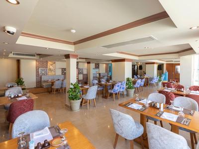 Jasna restauracja hotelowa z nakrytymi stolikami, niebieskimi krzesłami i roślinami jako dekoracją.