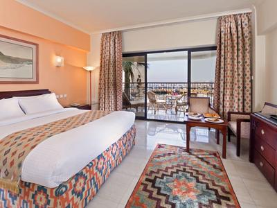 Lichte hotelkamer met groot bed, balkon met uitzicht op zee en moderne inrichting.