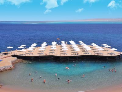 Plaża z parasolami i ludźmi pływającymi w czystej wodzie morskiej obok drewnianego pomostu.