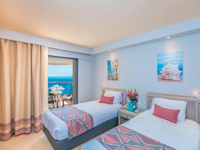 Hell eingerichtetes Hotelzimmer mit Twin-Betten und Meerblick vom Balkon.