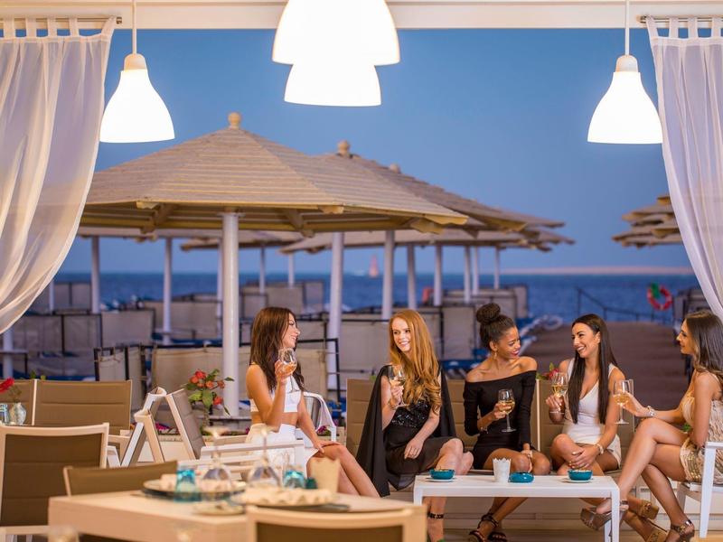 Gruppe junger Frauen entspannt sich abends an einem Strandrestaurant mit Blick aufs Meer.