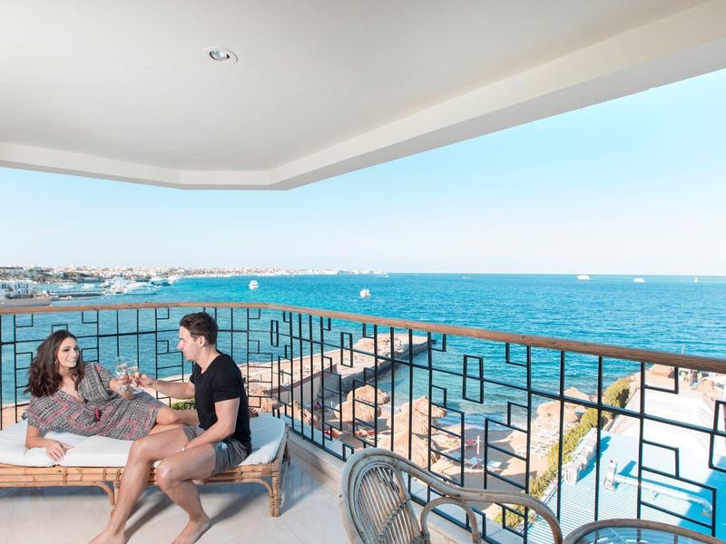 Balkon mit Sitzbereich und Blick auf das Meer und die Küste an einem sonnigen Tag.