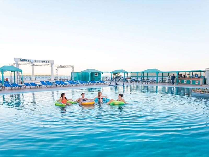 Kinder spielen im Pool eines Resorts mit klarer blauer Wasseroberfläche bei sonnigem Himmel.